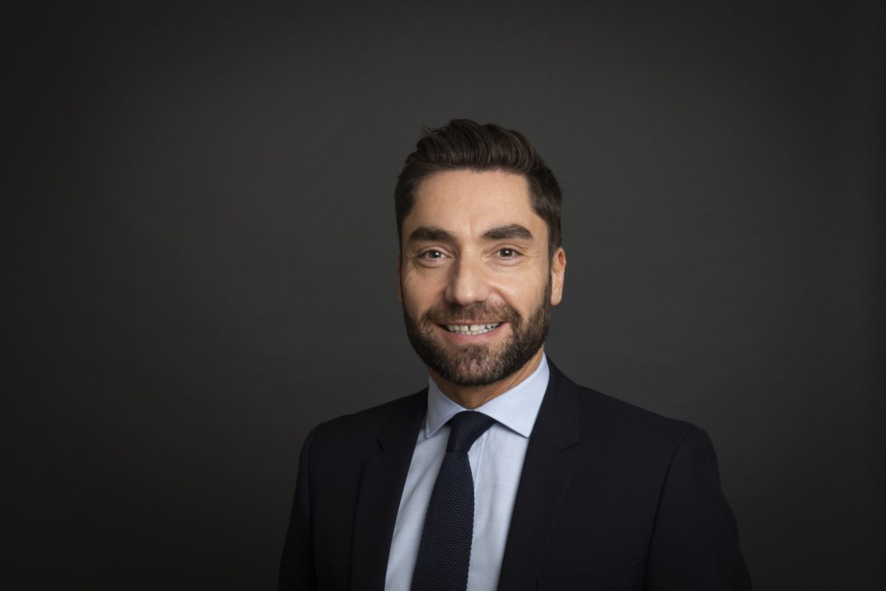 Portrait corporate en entreprise d'un homme souriant en veste et cravate sur fond gris foncé