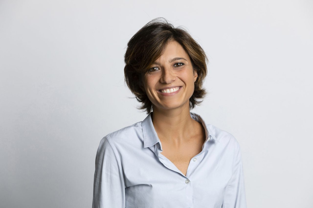Portrait corporate en studio sur fond clair d'une femme souriante cadré en plan buste. Elle porte un chemisier bleu ciel