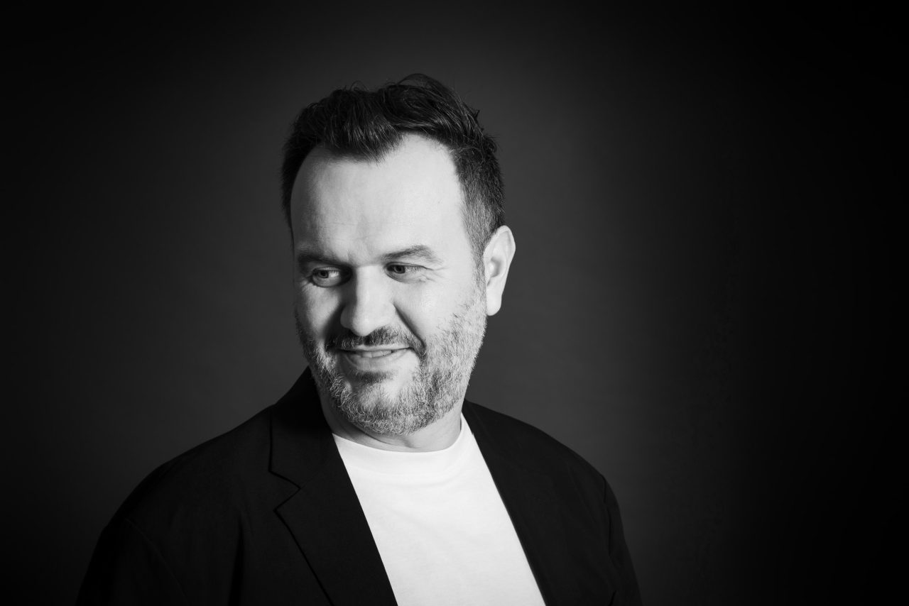 Portrait corporate noir et blanc d'un homme en T-Shirt et veste qui regarde vers le bas à sa droite. Photo de portrait en studio sur fond noir